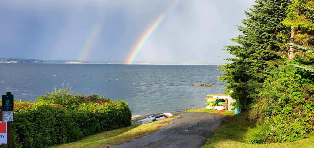 two rainbows over water, with trees and kayaks in foreground